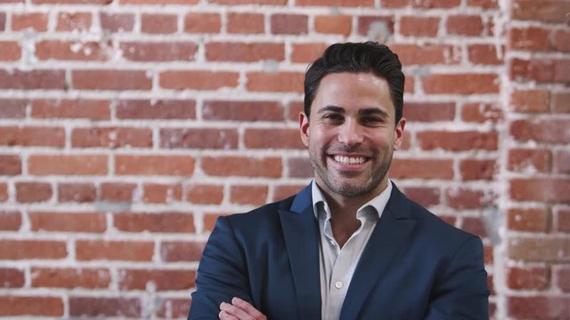 Portrait Of Smiling Mature Businessman Standing Against Brick Wall In Modern Office