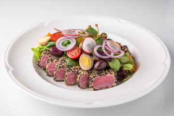 Delicious tuna salad in sesame, quail eggs, vegetables and dried olives. Nutritious healthy dish. Banquet festive dishes. Gourmet restaurant menu. White background.