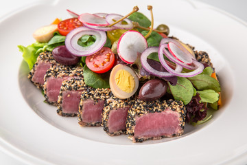 Delicious tuna salad in sesame, quail eggs, vegetables and dried olives. Nutritious healthy dish. Banquet festive dishes. Gourmet restaurant menu. White background.