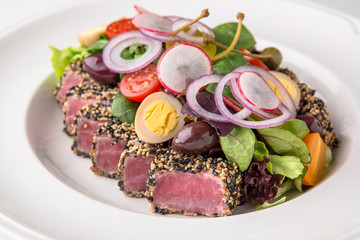 Delicious tuna salad in sesame, quail eggs, vegetables and dried olives. Nutritious healthy dish. Banquet festive dishes. Gourmet restaurant menu. White background.