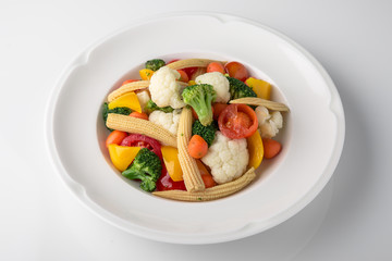 Fresh boiled vegetables: baby carrots, small corn dill, broccoli, cherry tomatoes, sweet peppers. Nutritious healthy dish. Banquet festive dishes. Gourmet restaurant menu. White background.