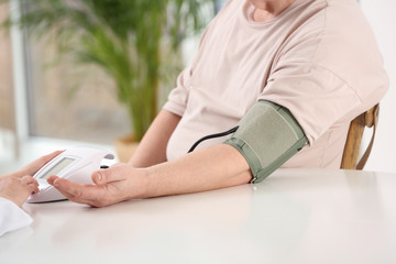 Nurse measuring blood pressure of elderly man indoors, closeup. Assisting senior generation