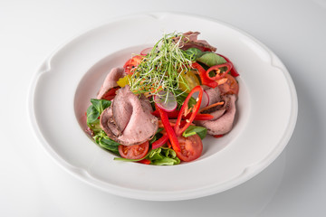 Salad of ham, prosciutto, pork or beef with vegetables, greens, berries and sauce. Nutritious, healthy dish. Banquet festive dishes. Gourmet restaurant menu. White background.