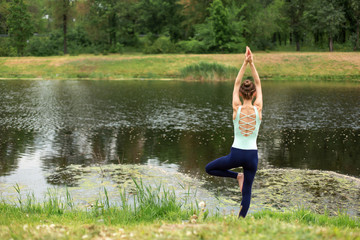 Slender young brunette yogi performs complex yoga exercise on green grass in the summer on a...