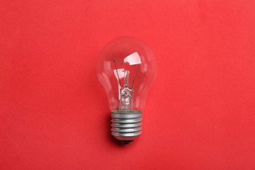 New incandescent lamp bulb on red background, top view