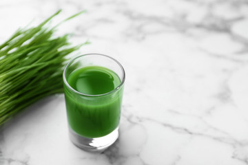 Glass of juice and fresh wheat grass on marble background. Space for text