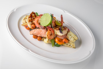 Luxurious seafood salad of shrimp, grilled salmon fillet, sea bream, grilled vegetables and lime. Banquet festive dishes. Fine dining restaurant menu. White background.