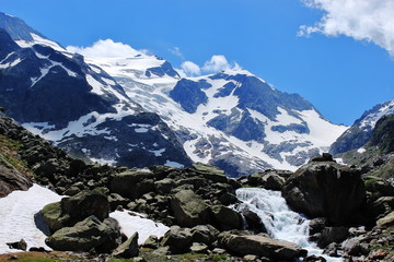 Cold glacial stream and mountain peaks covered with snow on summer sunny day. Tourist routes of Switzerland. Outdoor. Selective focus.