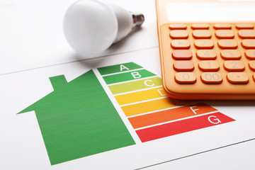 Energy efficiency rating chart, LED light bulb and calculator on white background, closeup
