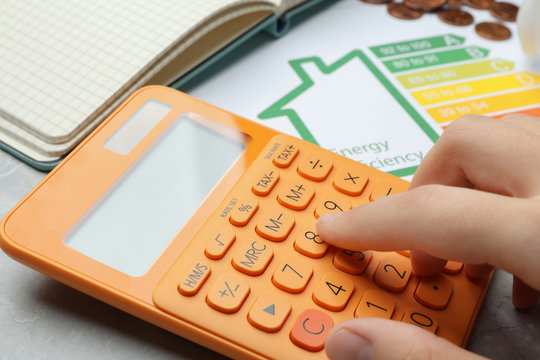 Woman with calculator and energy efficiency rating chart at table, closeup
