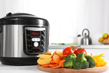 Modern multi cooker and wooden board with vegetables on white table in kitchen