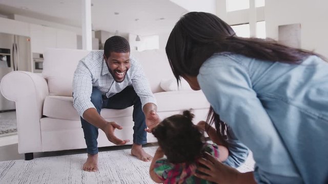 Parents At Home Encouraging Baby Daughter To Take First Steps