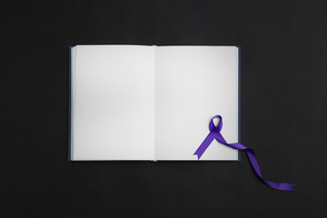 Purple awareness ribbon and open notebook on black background, top view with space for text