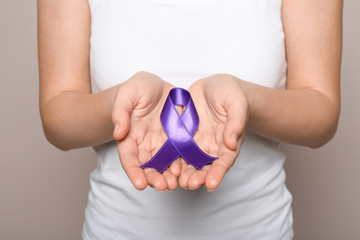 Woman holding purple ribbon on grey background, closeup. Domestic violence awareness
