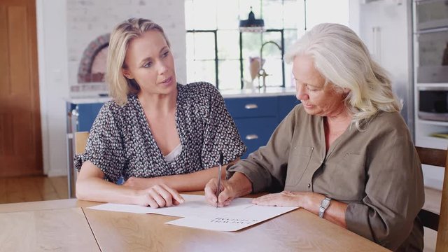 Female Friend Helping Senior Woman To Complete Last Will And Testament At Home
