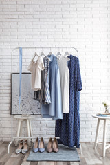 Wardrobe rack with women's clothes and different shoes at white brick wall in room