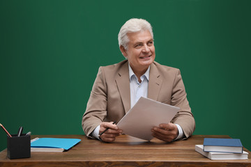 Portrait of senior teacher at table against green chalkboard