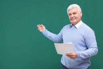 Portrait of senior teacher with paper at green chalkboard, space for text