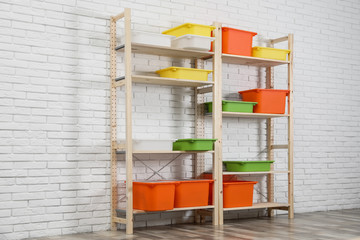 Wooden shelving units with colorful containers near white brick wall. Stylish room interior