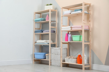 Wooden shelving units with clean towels and detergents in stylish room interior