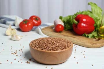 Bowl with uncooked buckwheat and vegetables on white wooden table indoors. Space for text