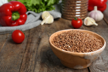 Ceramic bowl with uncooked buckwheat on wooden kitchen table. Space for text