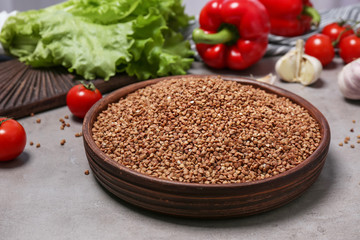 Ceramic plate with uncooked buckwheat and vegetables on grey kitchen table