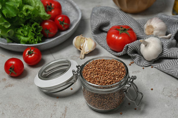 Glass jar with uncooked buckwheat on grey kitchen table