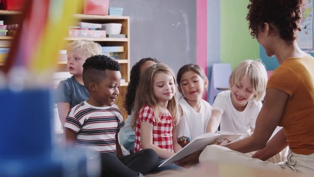 Female Teacher Reading Story To Group Of Elementary Pupils In School Classroom