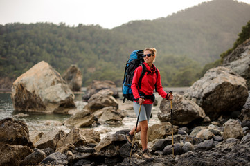 Woman with hiking equipment trekking through rocky coast