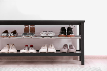Shoe rack with different footwear near white wall. Stylish hallway interior