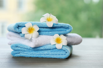 Pile of fresh towels and flowers on table against blurred background, space for text