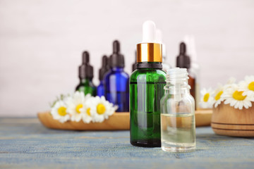 Bottles of chamomile essential oil and flowers on color table, space for text