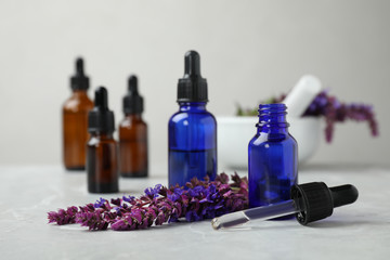 Bottles of sage essential oil and flowers on grey table