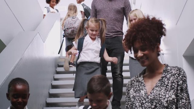 Teacher And Pupils Walking Down Stairs In Busy Elementary School Corridor