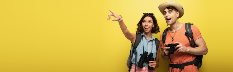 panoramic shot of two excited tourists looking away on yellow background