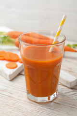 Glass of fresh carrot juice on white wooden table