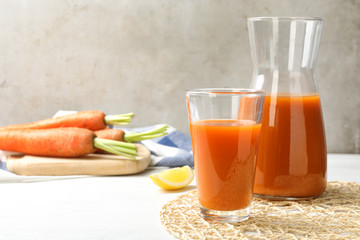 Glass and carafe with fresh carrot juice on white wooden table, space for text
