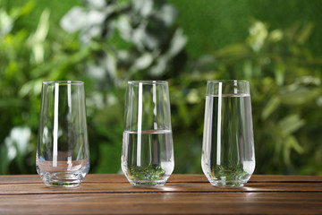 Empty, half and full glasses of water on wooden table against blurred background