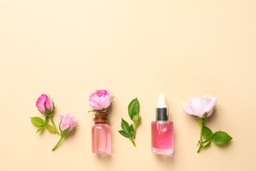 Fresh flowers and bottles of rose essential oil on color background, flat lay. Space for text