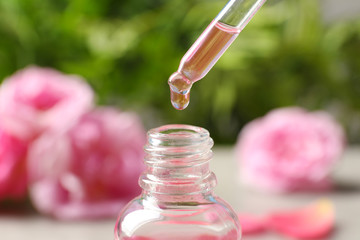 Dripping rose essential oil into bottle against blurred background