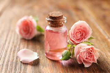 Fototapeta na wymiar Bottle of rose essential oil and flowers on wooden table