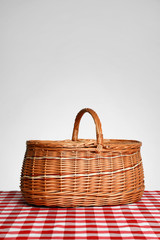Closed wicker picnic basket on checkered tablecloth against white background