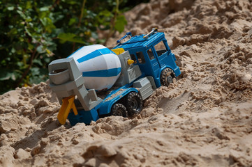 Toy concrete mixer on the background of a mountain of sand and bushes