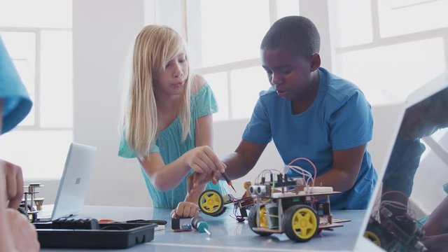 Two Students With Female Teacher In After School Computer Coding Class Learning To Program Robot Vehicle