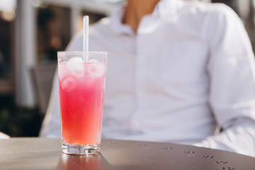 01.06.2019 Odessa, Ukraine: Young attractive man holds a glass of summer refreshing drink in his hand, enjoying a rest on the summer terrace of the cafe