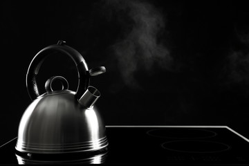 Modern kettle with whistle on stove against black background, space for text