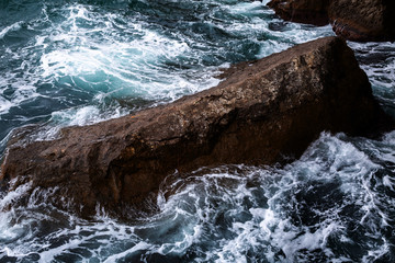 Danger sea wave crashing on rock coast with spray and foam before storm