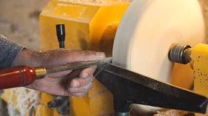 Woodworker handles wood by bench. Making beautiful wooden handmade dish. Craftsman works with workpiece in workshop. Creation of unusual platter. Carpenter cuts wood by graver.