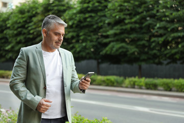 Fototapeta premium Portrait of handsome mature man using mobile phone outdoors. Space for text